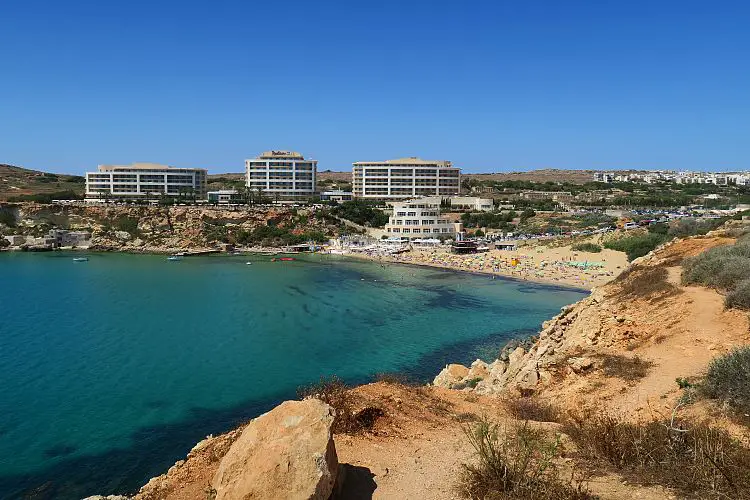 Der Sandstrand und die Klippen an der Golden Bay im Norden von Malta. Der Strand ist goldgelb gefärbt, oberhalb des Strandes steht ein großes Hotel.