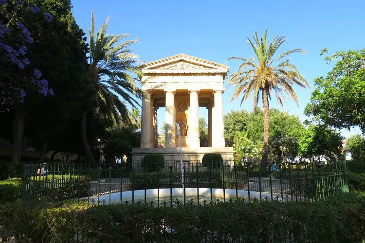 Das Bild zeigt einen im römischen Stil gestalteten Tempel und einen Springbrunnen im mit Palmen und Sträuchern bewachsenen Lower Barrakka Garden in Maltas Hauptstadt Valletta. 