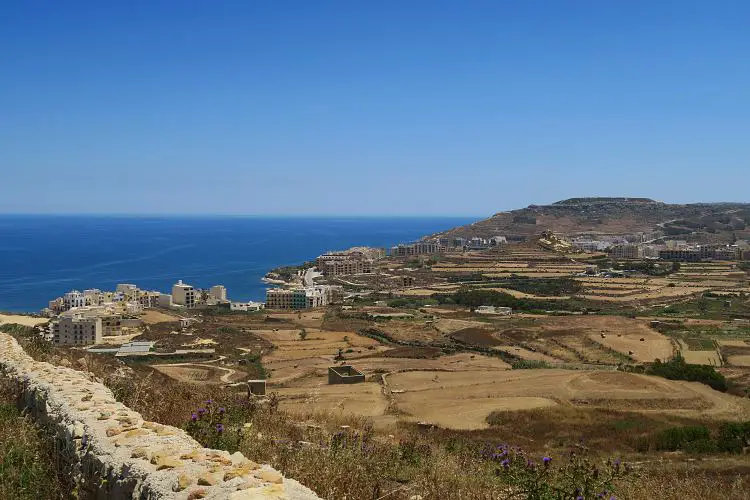 Blick vom auf einen Hügel liegenden Ort Zebug auf den am Meer gelegenen Ort Marsalforn auf Maltas Nachbarinsel Gozo. Im Hintergrund ist das Meer zu sehen. 