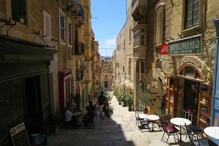 Eine schmale Gasse führt über Treppen zum Meer in Maltas Hauptstadt Valletta hinunter. Auf der linken und rechten Seite der Gasse befinden sich kleine Restaurants. 