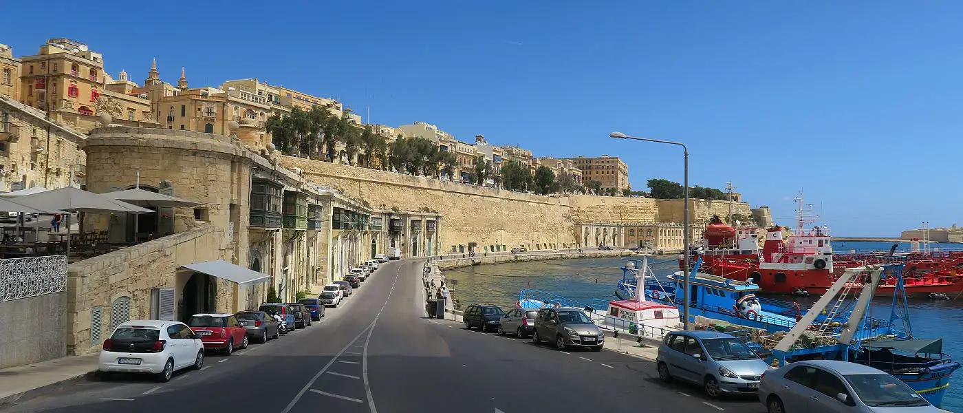 Eine Straße in Valletta, der Hauptstadt von Malta, in dem ein Mietwagen am Meer geparkt ist.