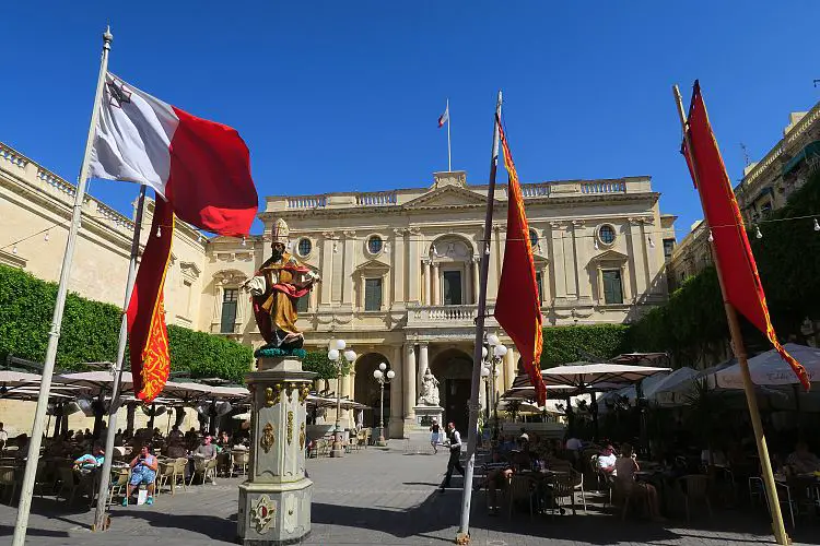 Der Platz vor der Nationalbibliothek von Malta mit einem Gastgarten und maltesischen Flaggen.