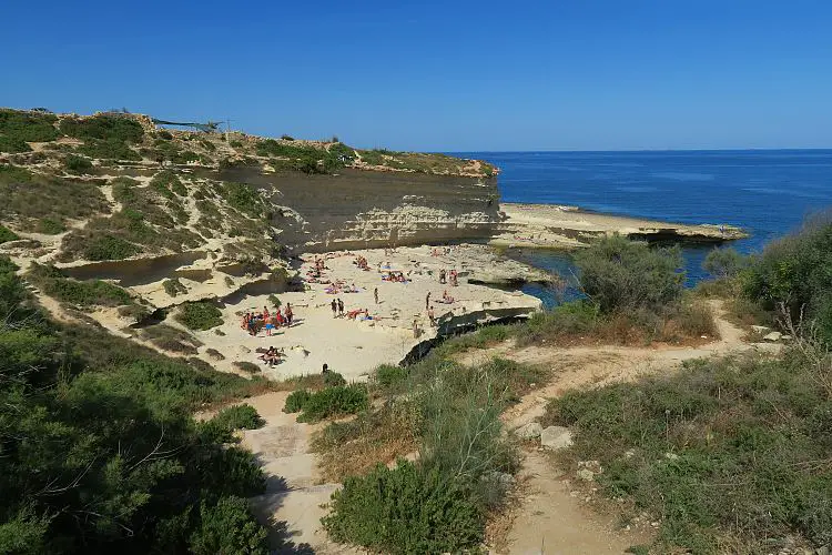 Der mit grünen Wiesen umgebene Weg zum St. Peter´s Pool im Frühling. Es schwimmen Menschen im Meer.