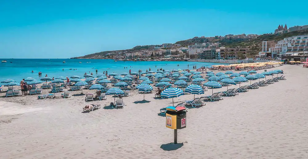 Der Mellieha Bay Sandstrand mit Sonnenschirmen, Strandliegen und Hotels